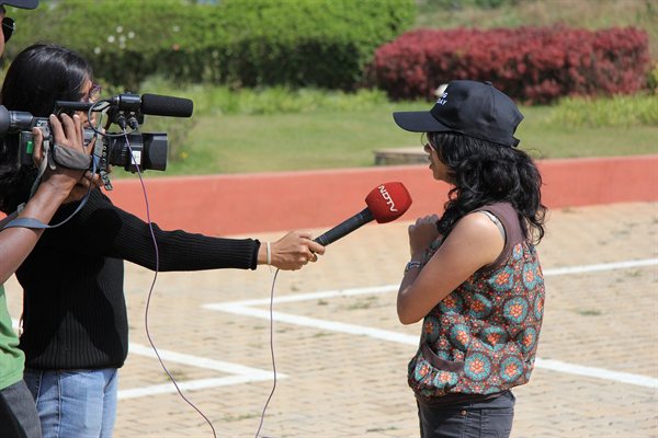 An NDTV crew with a camera and a branded microphone interviewing a woman outdoors in Bengaluru