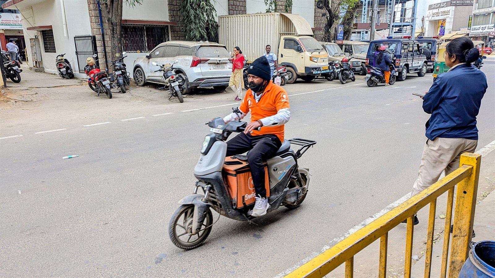 A Swiggy delivery rider in an orange uniform on an electric scooter on a city street